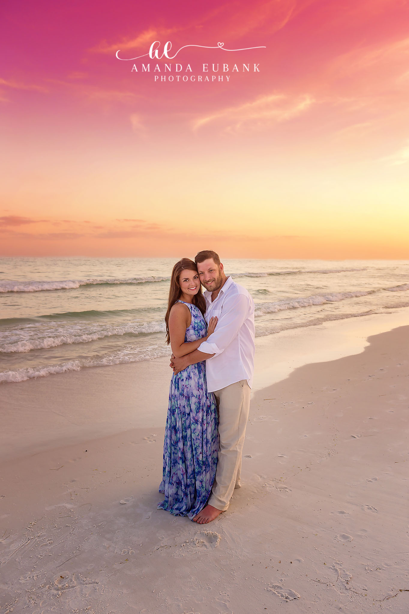 Seaside engagement photographer captures couple embracing on beach at vibrant pink sunset