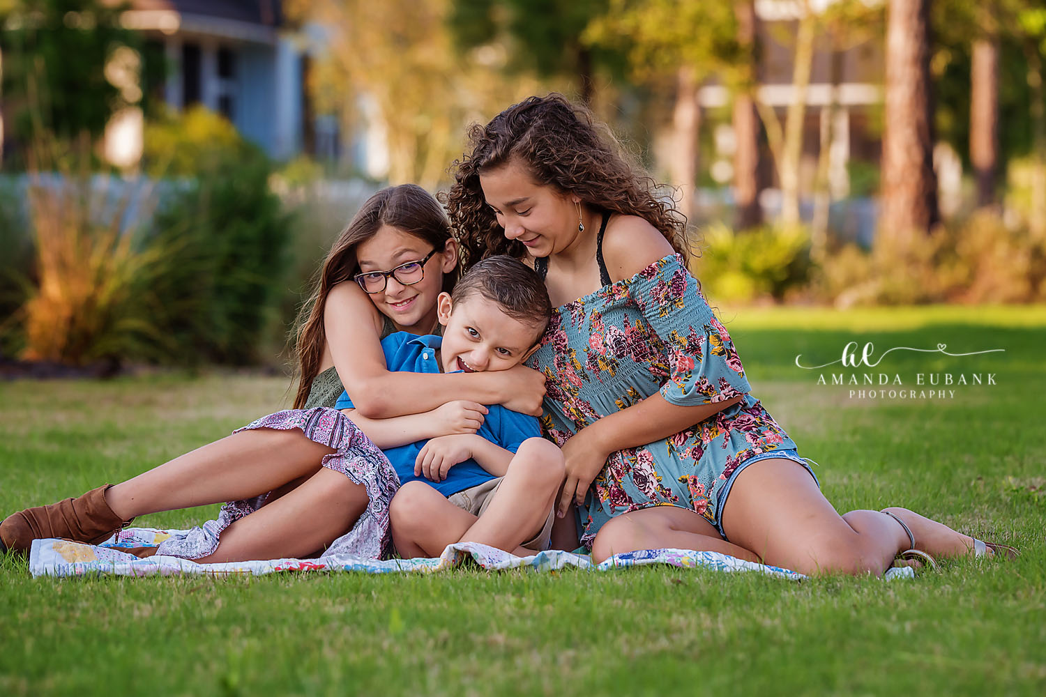 Seaside family photographer captures three siblings in group hug on grass with golden hour light