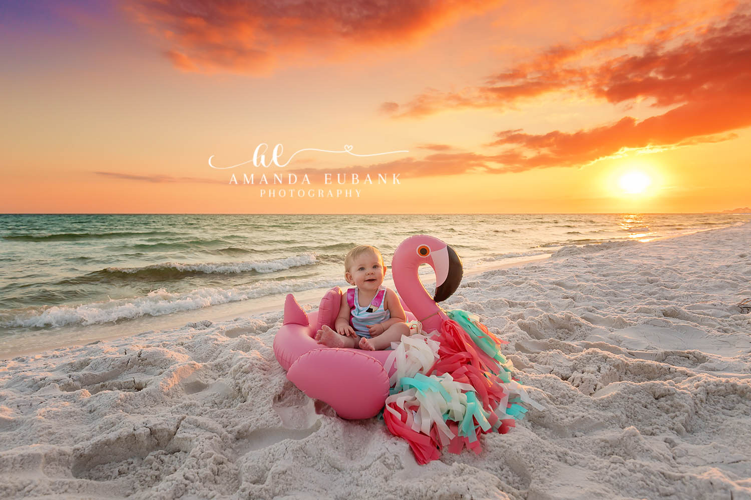 Seaside baby photographer captures baby in flamingo float on beach at horizon sunset