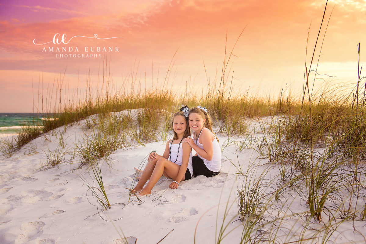 Seaside family photographer captures two sisters in dunes at painted pastel sunset