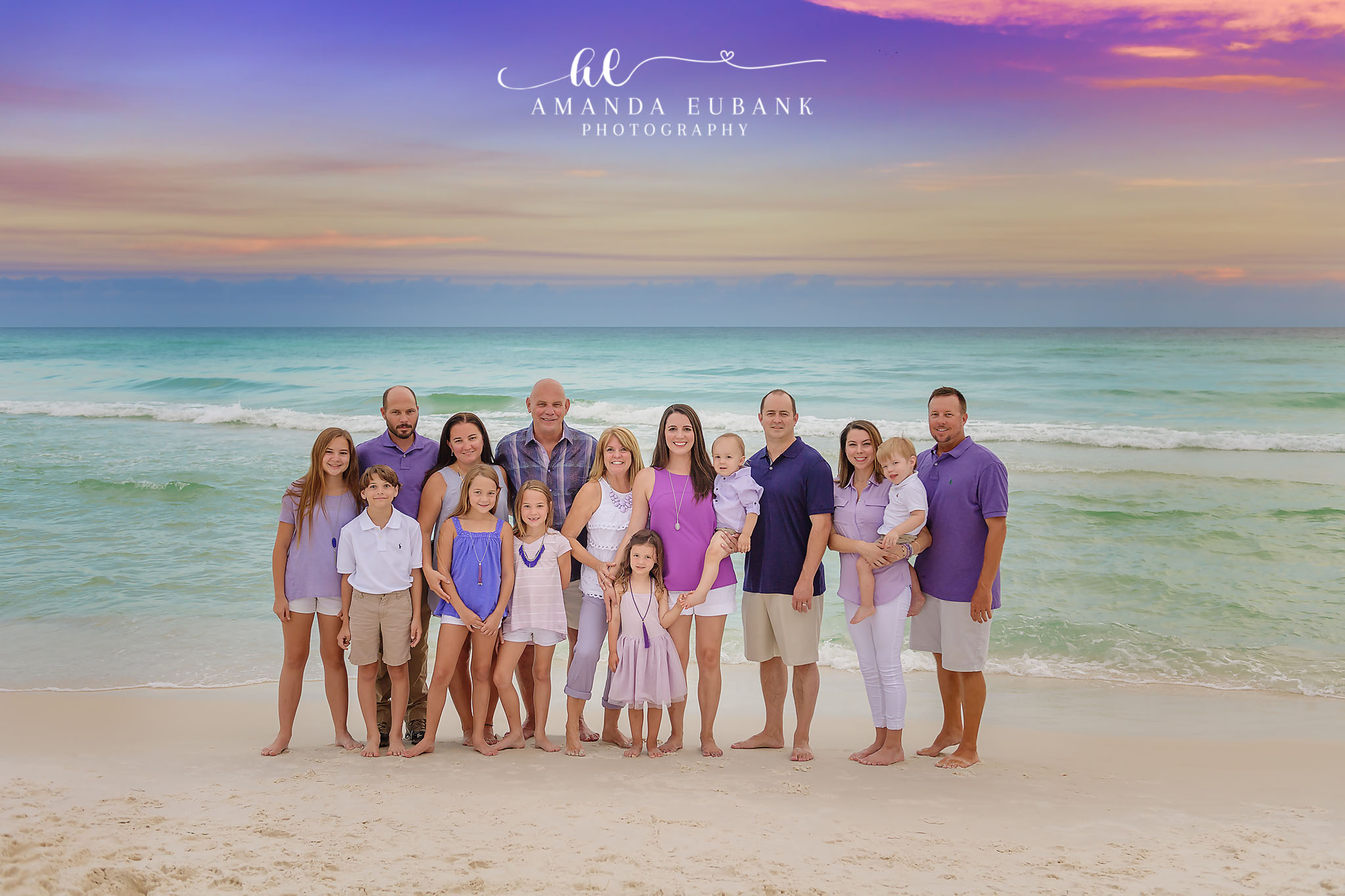 Seaside family photographer captures extended family in purple and white on beach at pastel sunset