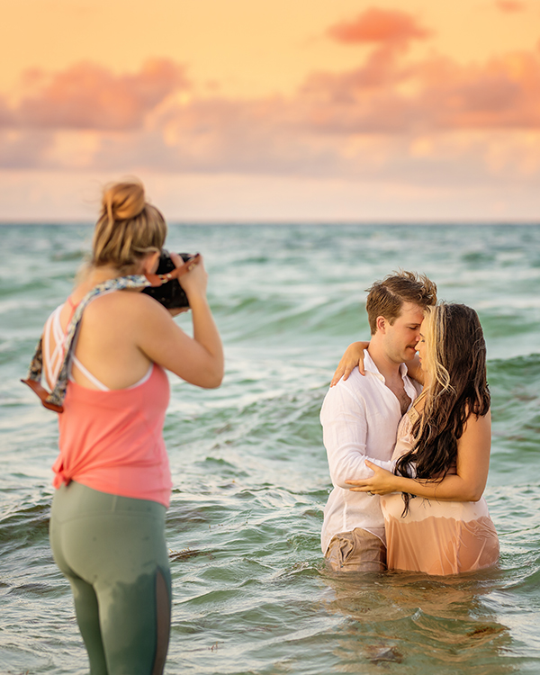 Seaside photographer behind the scenes capturing engagement couple in surf at sunset