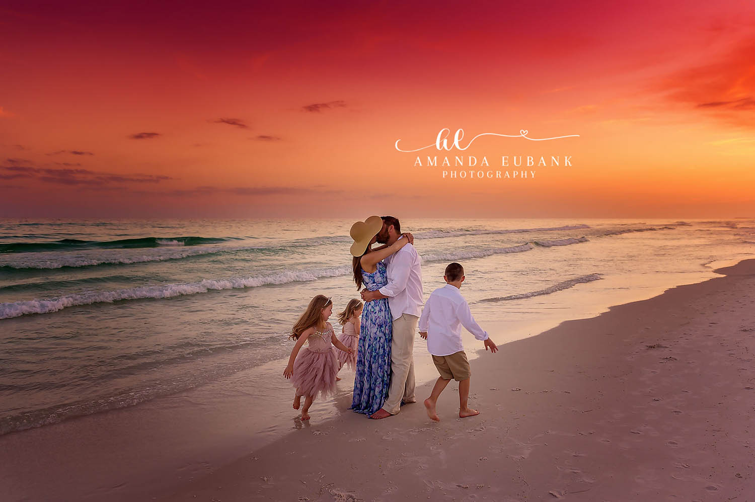 Seaside family photographer captures family of five with kissing parents at fiery sunset