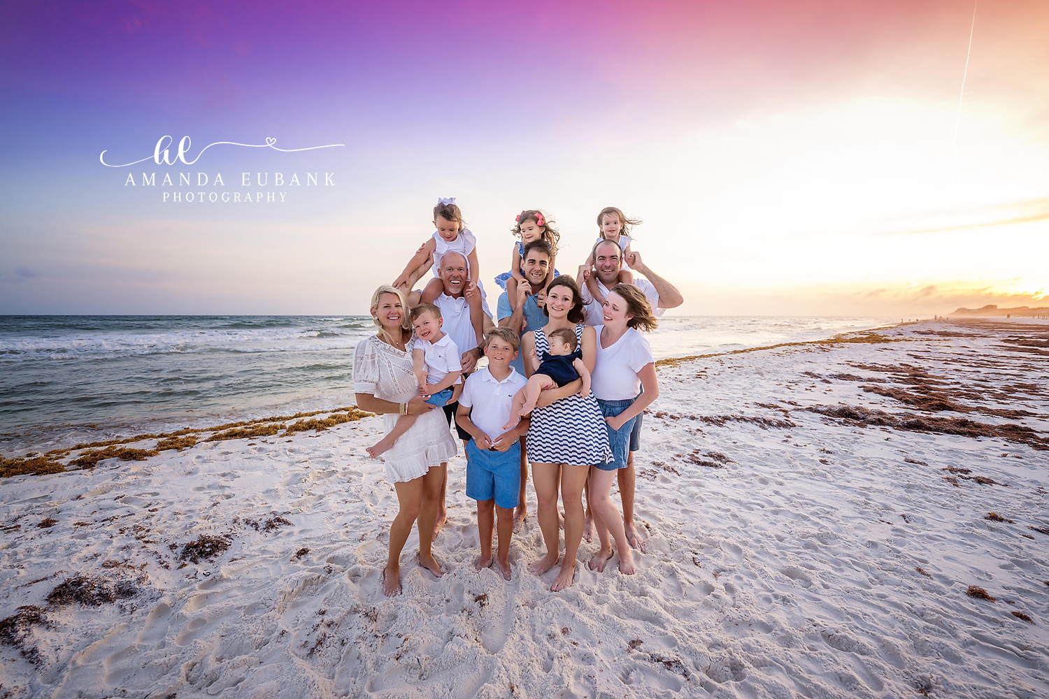 Seaside family photographer captures large family with kids on shoulders at purple sunset
