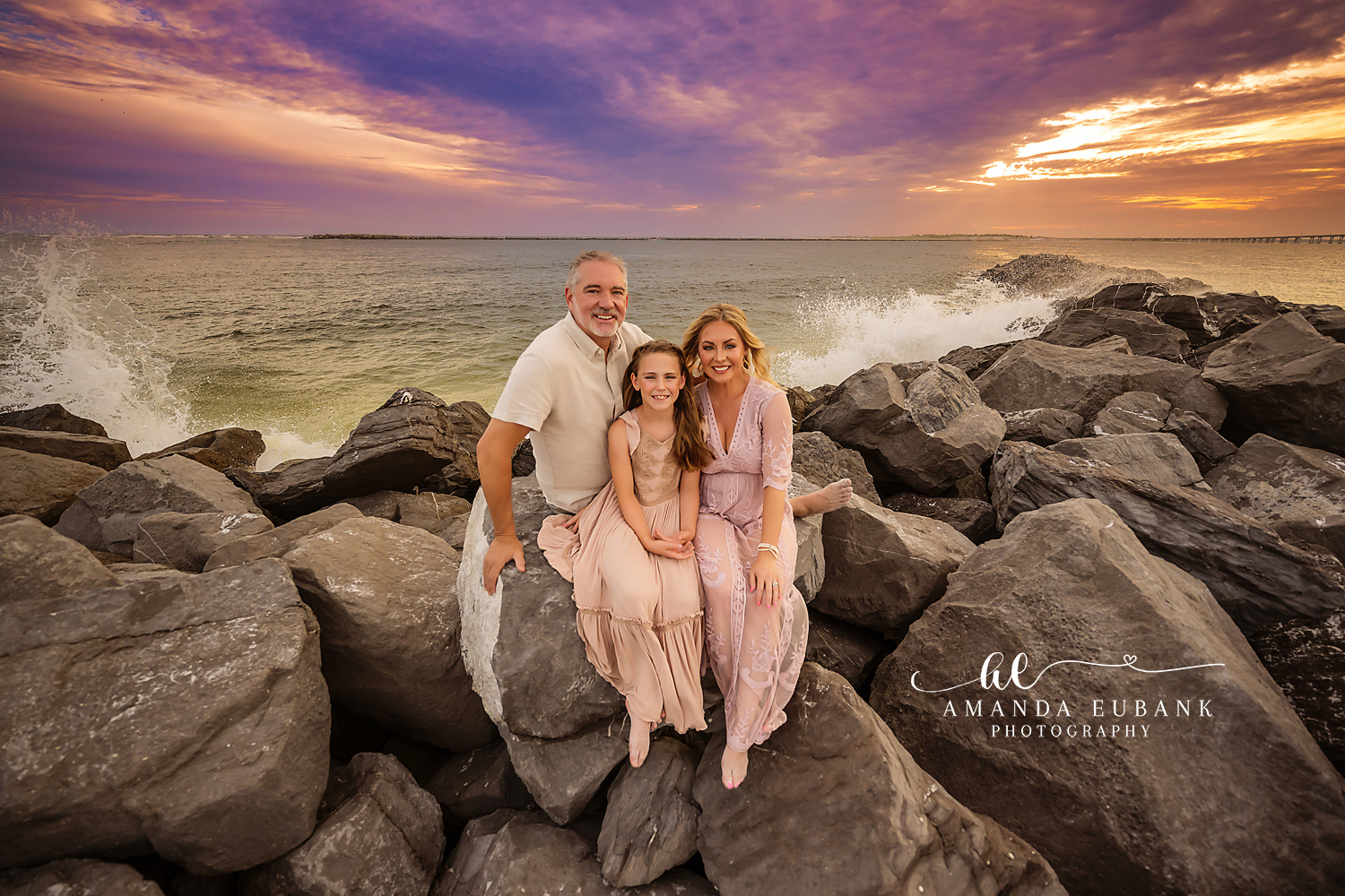 Seaside family photographer captures family of three on rocky jetty at golden sunset