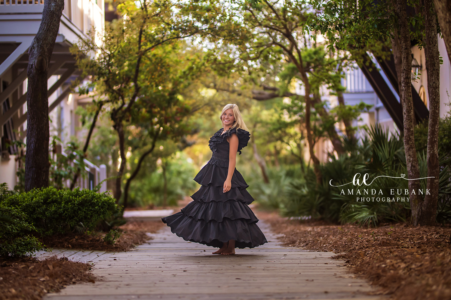 Seaside senior photographer captures high school senior in black ruffled gown on a tree-lined path
