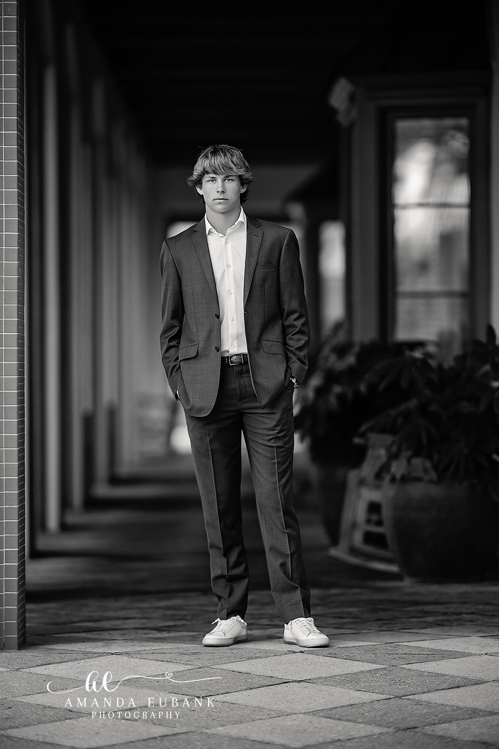 Seaside senior photographer captures black and white portrait of male senior in suit standing in columned corridor