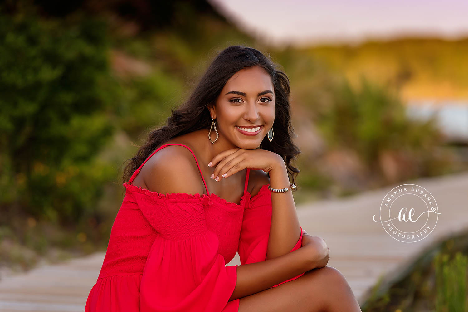 Seaside senior photographer captures close-up of brunette senior in red dress with teardrop earrings on beach